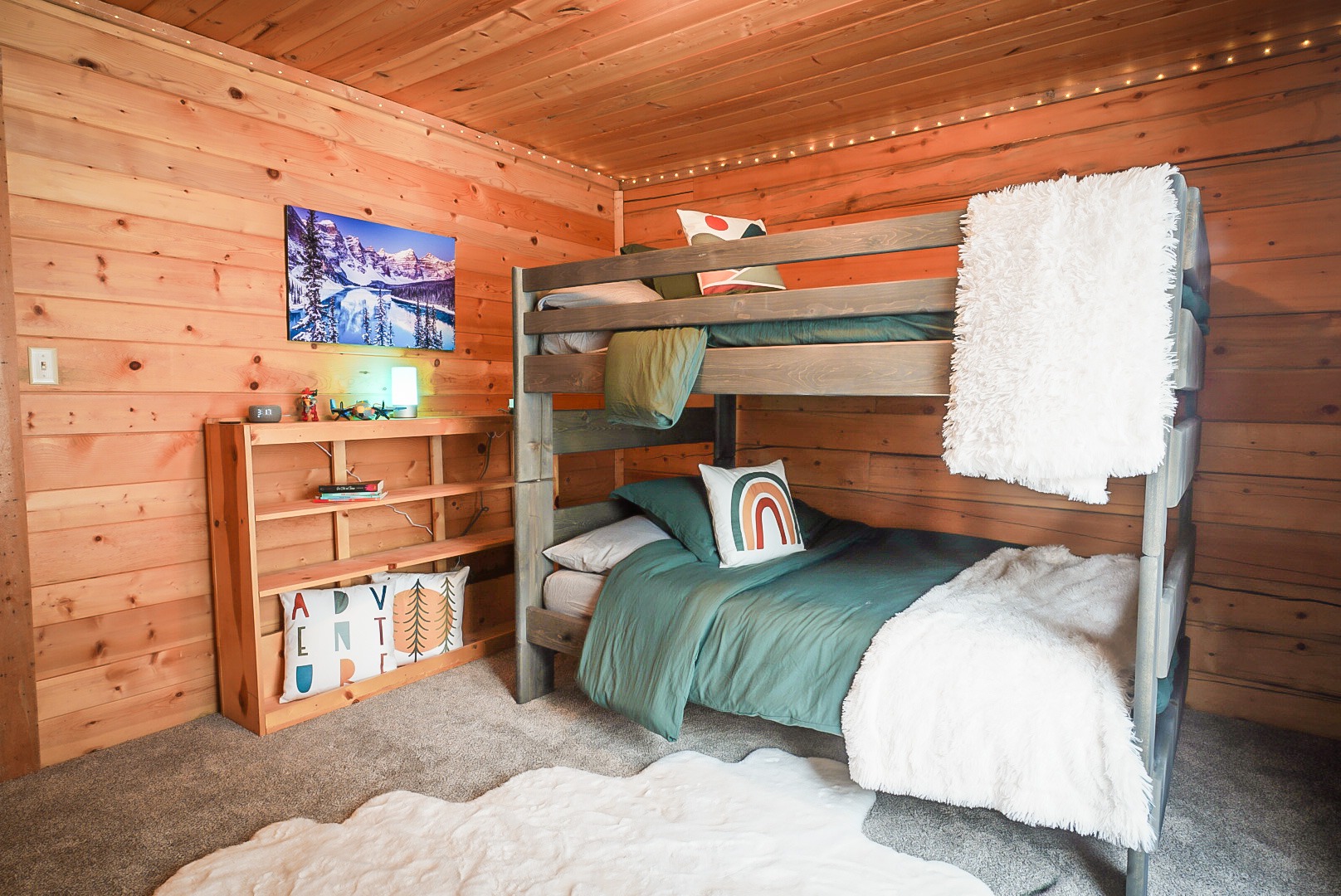 Bunk room with wood bunks, green bedding, bean bag chairs and a game corner under a pine ceiling