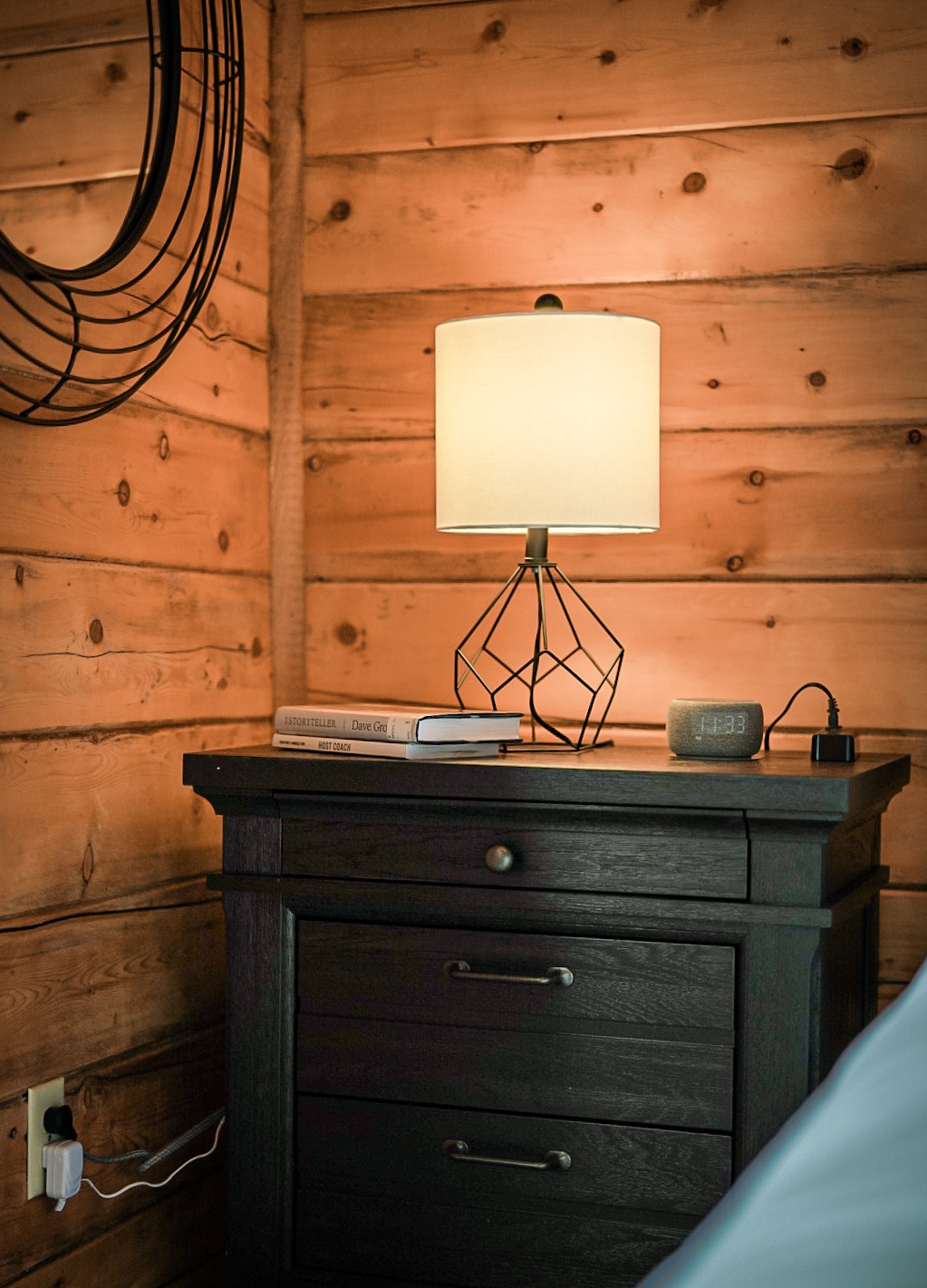 Nightstand with a reading lamp and clock against knotty-pine walls