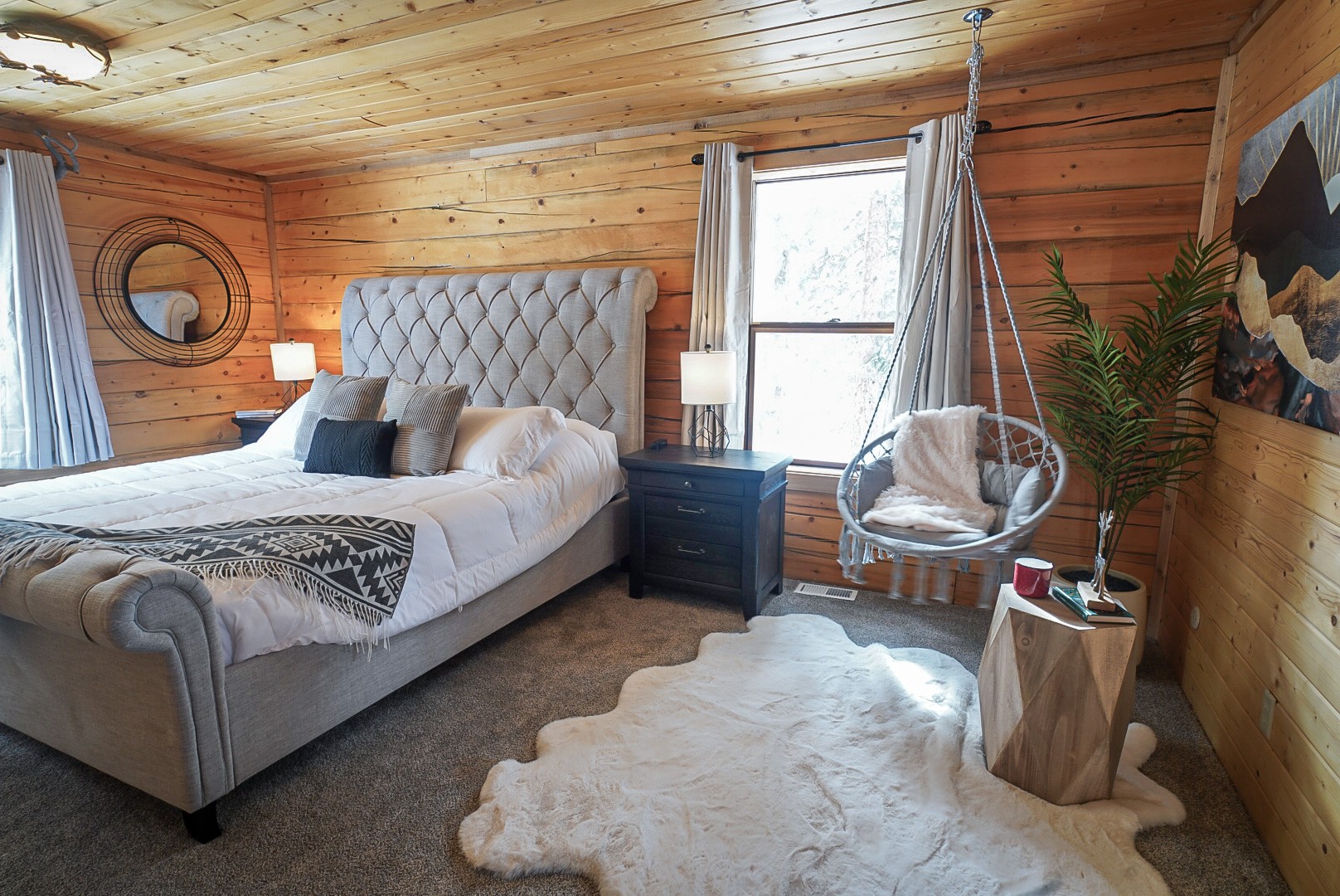 Main-floor primary suite with a king bed, gray upholstered headboard and pine forest views